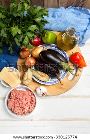 Minced meat, eggplants, onion, garlic, pepper, cheese, parsley and olive oil on a white table