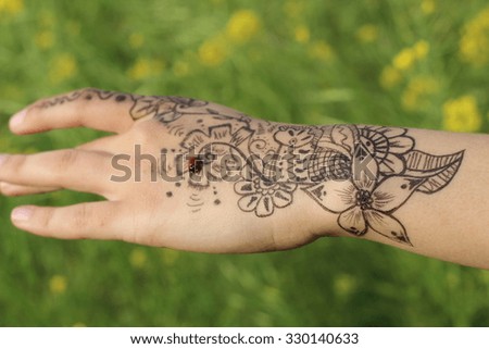 Henna on girl hand on greenish yellow background and ladybug