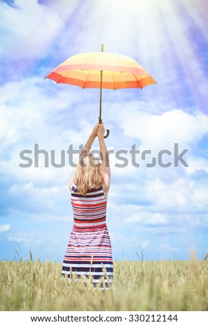 Picture of beautiful young lady rising colorful umbrella on golden wheat field. Backview of pretty girl in striped dress on sunrays countryside background.