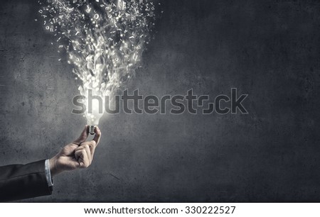 Hand holding glass glowing lightbulb on cement background