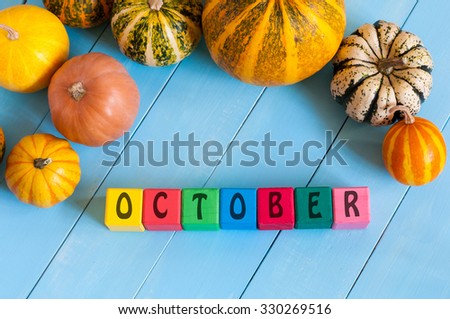 Autumn, many-coloured pumpkins frame, the word October on toy cubes, with light wooden background