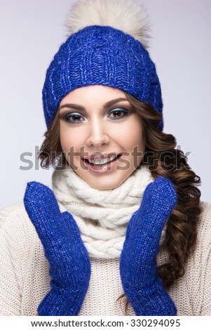 Beautiful girl with a bright make-up, curls and a smile in winter blue  knit cap. Warm winter image. Beauty face. Picture taken in the studio.