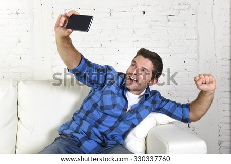 young attractive 30s man taking selfie photo or self video with mobile phone at home sitting on couch smiling happy in use of technology and image concept