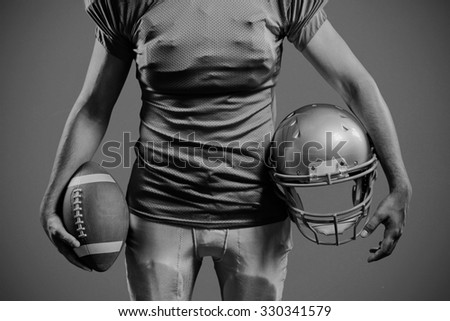 Mid section of sportsman holding American football and helmet against red background