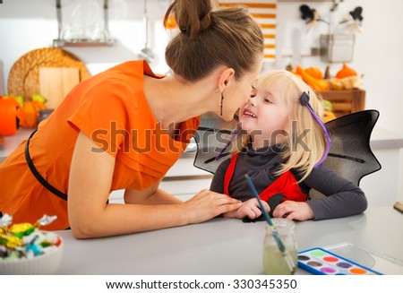 Eskimo kisses between a young mother and her halloween dressed blond daughter, while standing in decorated kitchen for party. Traditional autumn holiday