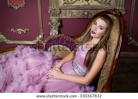 portrait of young beautiful girl in long pink dress sitting on the retro sofa
