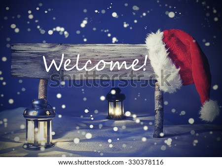 Vintage Wooden Christmas Sign And Santa Hat With White Snow. English Text Welcome For Seasons Greetings. Blue Silent Night With Snowflakes. Lantern And Candlelight