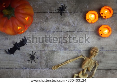 Halloween concept with a pumpkin,skeleton,candles and toy spider on a cobweb wood background