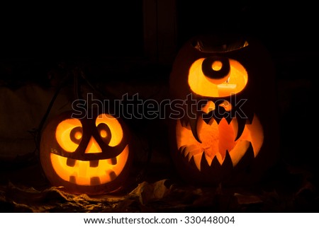Photo composition from two pumpkins on Halloween. The madman and a Cyclops of pumpkin stand against an old window, leaves and candles.