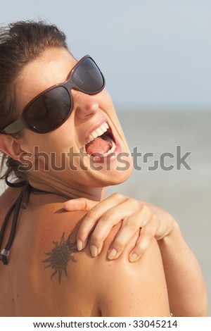 Young woman on a beach is holding her back in pain. She has a sunburn.