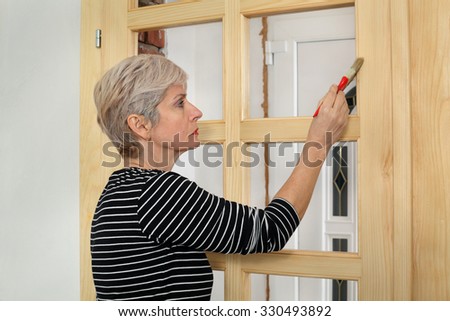 Adult female worker painting new wooden door with paintbrush