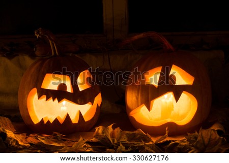 Photo composition from two pumpkins on Halloween. Embittered and frightened pumpkins stand against an old window, leaves and candles.