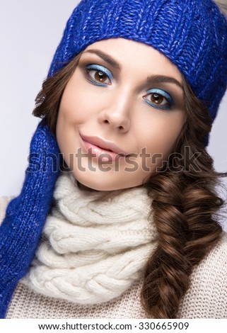 Beautiful girl with a gentle make-up, curls and a smile in winter blue  knit cap. Warm winter image. Beauty face. Picture taken in the studio.