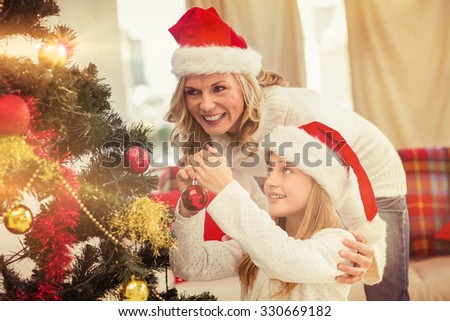 Festive mother and daughter decorating christmas tree at home in the living room