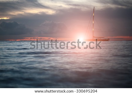 Beautiful calm evening seascape with yacht sailing in dark blue seaways under bare poles floating in the sea in rays of amazing red sunset on horizon against red and blue cloudy sky, horizontal photo