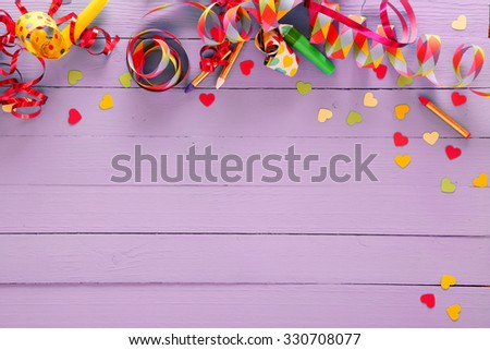 Colorful festive party border and background with with vibrant multicolored streamers, matches and confetti on a rustic lilac wood background with copyspace for your greeting or invitation