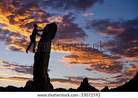 Climber is silhouetted on the edge as he struggles to the summit of a needle thin, rock spire.