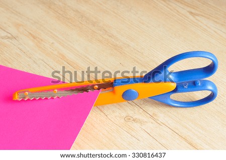 A colorful scissor that cut a zigzag pattern with a pink paper illustrating the pattern 