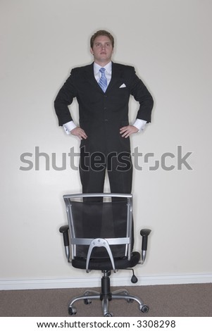 Businessman standing on his chair in confidence showing his strength to rise above the rest in his office
