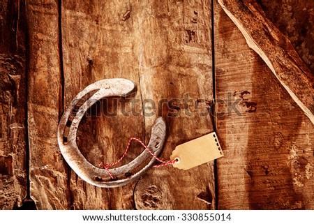 Lucky horseshoe background with an old shiny metal horseshoe tied with a blank gift tag lying on old rustic wood with a diagonal bar in the corner, overhead view