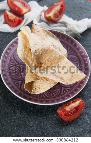 Fresh homemade papad with sliced tomatoes, close up on stone cutting board background