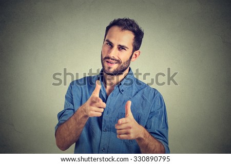 Portrait handsome young smiling man giving thumbs up pointing fingers at camera, picking you as friend isolated on grey wall background. Positive human emotion facial expression sign body language