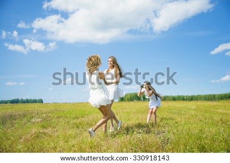 Three girlfriend reel round circling in dance in the summer daisy summer field against blue sky with white clouds. 3 caucasian woman play outdoor in short stylish dress Photographer makes the photo