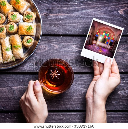 Hands with photo of Rajasthan palace and badyan tea near Turkish baklava on wooden background  