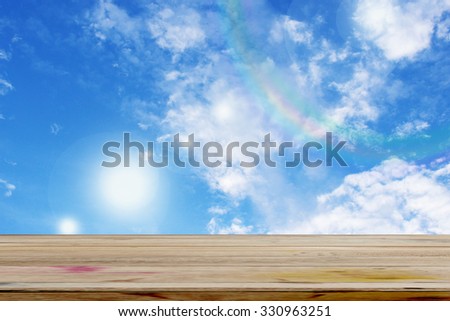 Empty wooden deck table over rainbow on the blue sky 