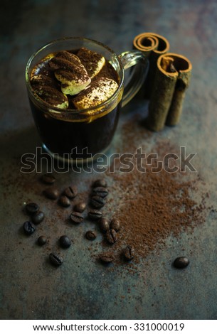 Cup of black coffee and marshmallows with chocolate over them, and coffee beans on the stone dark background. Toned picture