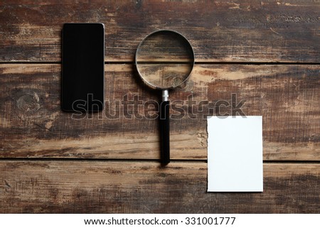 mobile phone, magnifier and sheet of paper on a wooden table. composition about searching