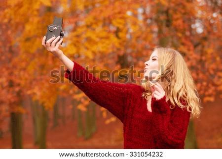 Pretty woman in fall forest park taking selfie self photo with old vintage camera. Gorgeous young girl passionate photographer blowing kiss. Autumn winter photography.