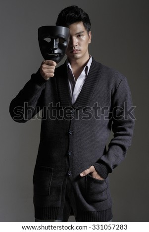 Asian man in yarn cardigan holding a black mask