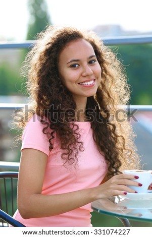 Pretty young woman in pink dress drinking coffee at summer terrace