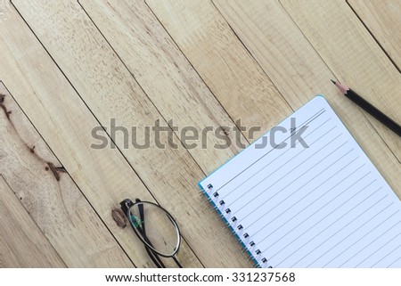  notebook with pencil and glasses on wooden table.