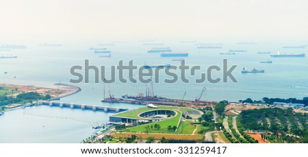 Many commercial cargo ships of various sizes, moored in a harbor, stretching to the hazy horizon.
