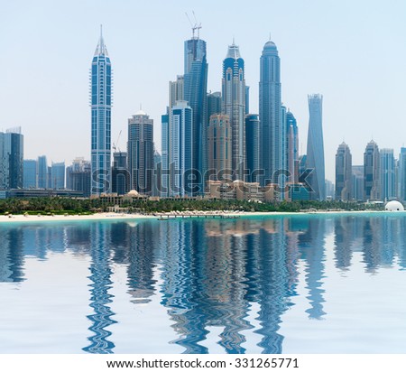 Stylish and contemporary architecture of a modern, metropolitan skyline, towering over a tropical beach and reflecting in a calm sea.