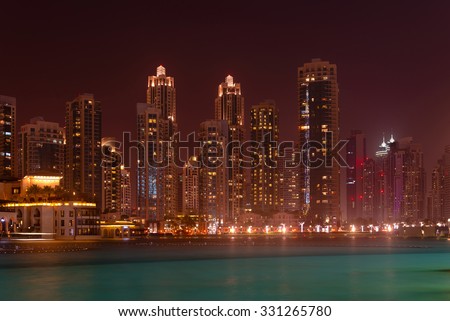 Dramatically lit nighttime skyline of a major metropolitan city, standing over a beautiful, tropical sea.