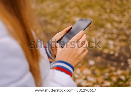 The girl holds a mobile phone in hand outdoor