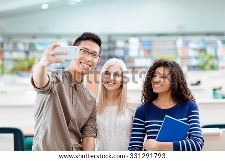 Smiling multi ethnic students making selfie photo on smartphone in the university library