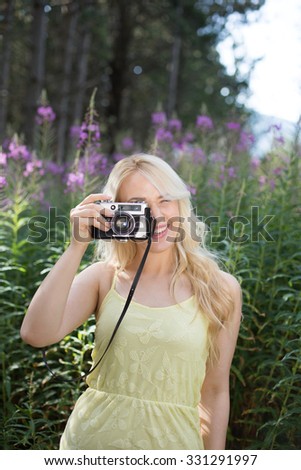 Outdoor summer smiling lifestyle portrait of pretty young blonde woman having fun in the nature, camera travel photo of photographer Making pictures in hipster style