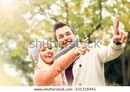 A picture of a young romantic couple pointing at something in the park in autumn
