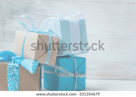 Four gift boxes in wrapping paper with ribbons lying on a white wooden background, selective focus, toned photo