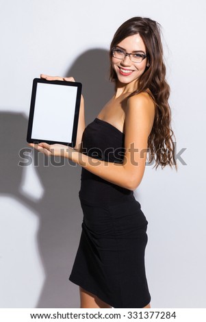  stylish girl in a black business dress and sunglasses standing on a white background with a snow-white smile, smiling, picture with depth of field, selective focus on the tablet, instagram filter