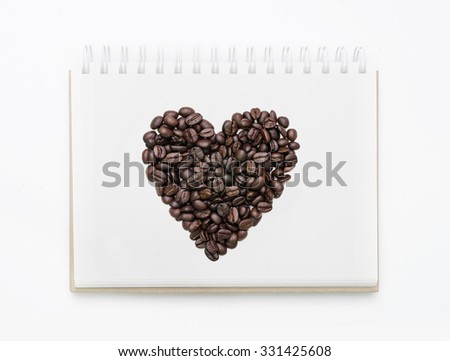 Heart shape roasted coffee beans on white notebook background.