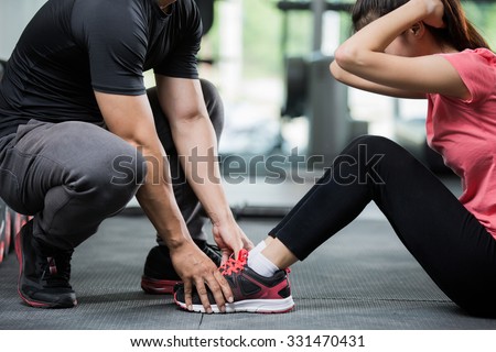 Trainer holding a woman in the leg exercise by Sit-up. Royalty-Free Stock Photo #331470431