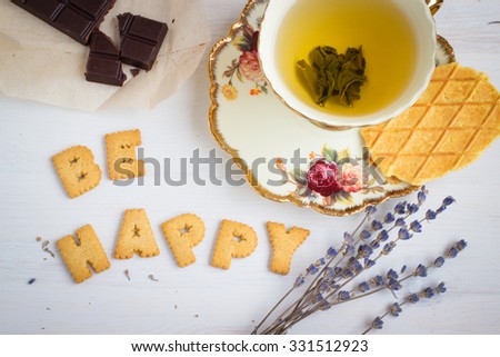 Quote BE HAPPY. Still life image with biscuits, organic chocolate and vintage cup of green tea white wooden background. Top view collage made of biscuits. Retro toned and instagram filtered image. Royalty-Free Stock Photo #331512923