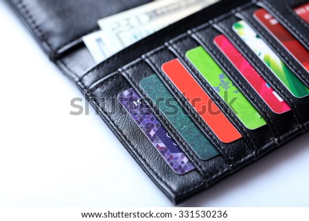 Black leather wallet with colourful credit cards and money on white background, close up