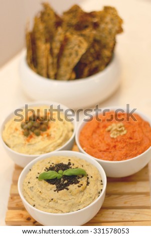 Three bowls with different dips: tuna dip, red pepper dip and hummus dip. Defocused crackers in the background. 