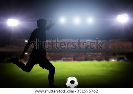 silhouette of a player shooting football on goal. Lights on the football stadium at night.